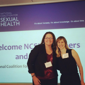 NSVRC's Jennifer Grove (left) and PreventConnect's Ashley Maier (right) standing and smiling in front of a powerpoint slide projected on a screen that reads "National Coalition for Sexual Health"