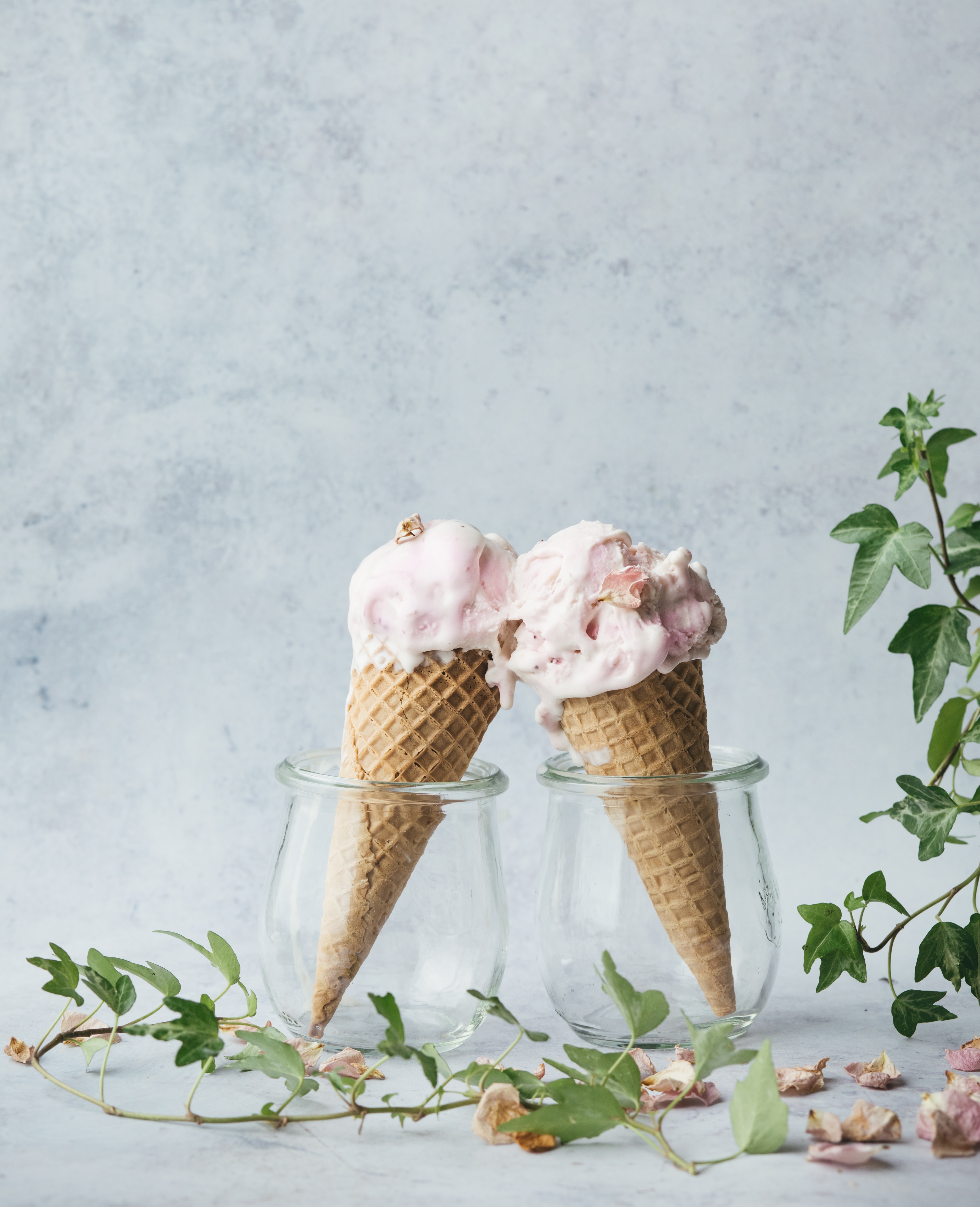 Two ice cream cones sit in glasses and touch each other