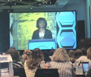 A photo of Dr. Anita Hill on a projection screen. Dr. Hill is behind a podium. 