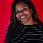 Image of Aisha Shillingford. A black woman with locs and a nose ring smiles into the camera. She's wearing a black shirt with white stripes and is in front of a red background