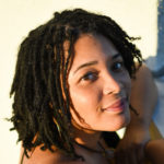 Image of Tonjie Reese. A black woman with shoulder length locs locks over her shoulder to smile at the camera